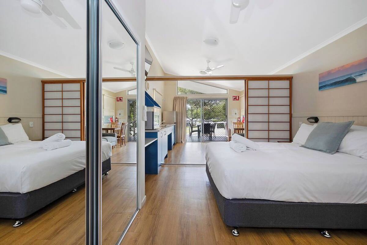 Ein modernes Hotelzimmer mit zwei Betten, einer Küchenzeile und einer Glastür zum Balkon.