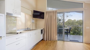 A modern kitchen with white cabinets, a built-in microwave, and a flat-screen TV. - Reflections Brunswick Head - Holiday Park (Brunswick Heads)