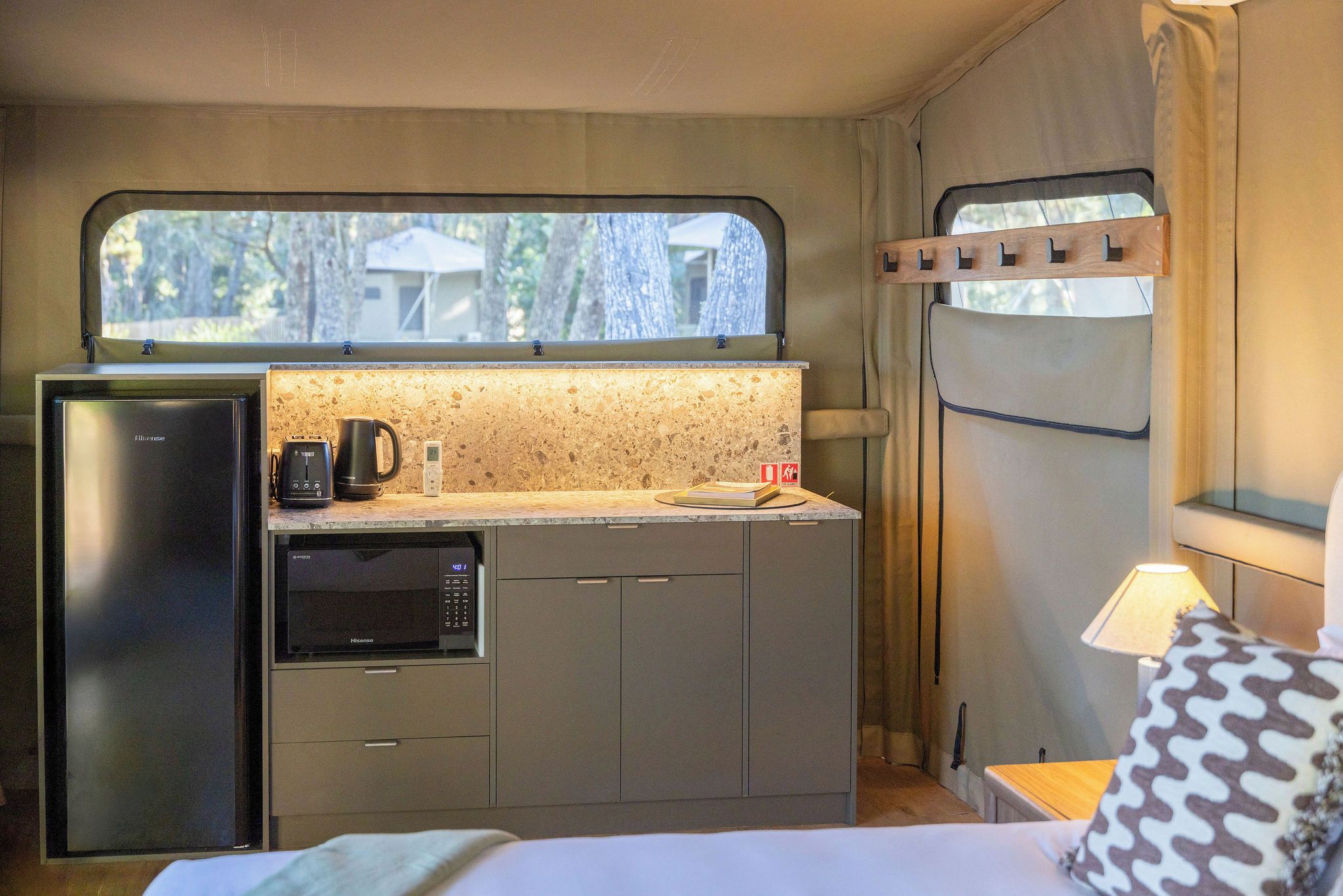 A compact kitchenette with a microwave, toaster, and kettle, a small refrigerator, and a window with a view of trees.