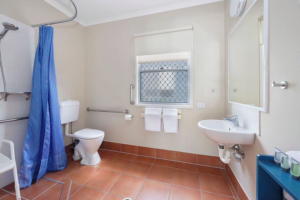 A bathroom with a toilet, sink, shower, and a window with a metal grid.