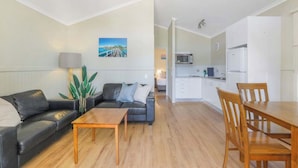 A compact living space with a sofa, a dining table, and a kitchen area. - Reflections Brunswick Head - Holiday Park (Brunswick Heads)