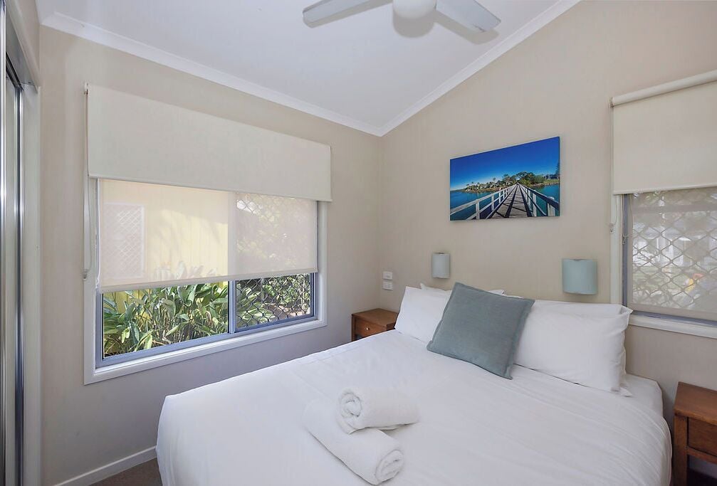 Un dormitorio con una cama grande, dos mesitas de noche, un ventilador de techo y una ventana con vistas a zonas verdes.