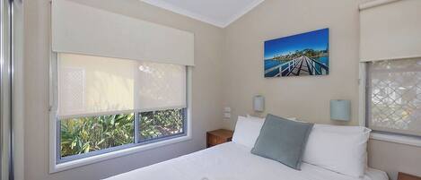 Un dormitorio con una cama grande, dos mesitas de noche, un ventilador de techo y una ventana con vistas a zonas verdes.