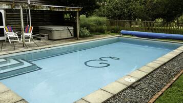 Una piscina rettangolare con solarium piastrellato, una vasca idromassaggio e due poltrone prendisole.