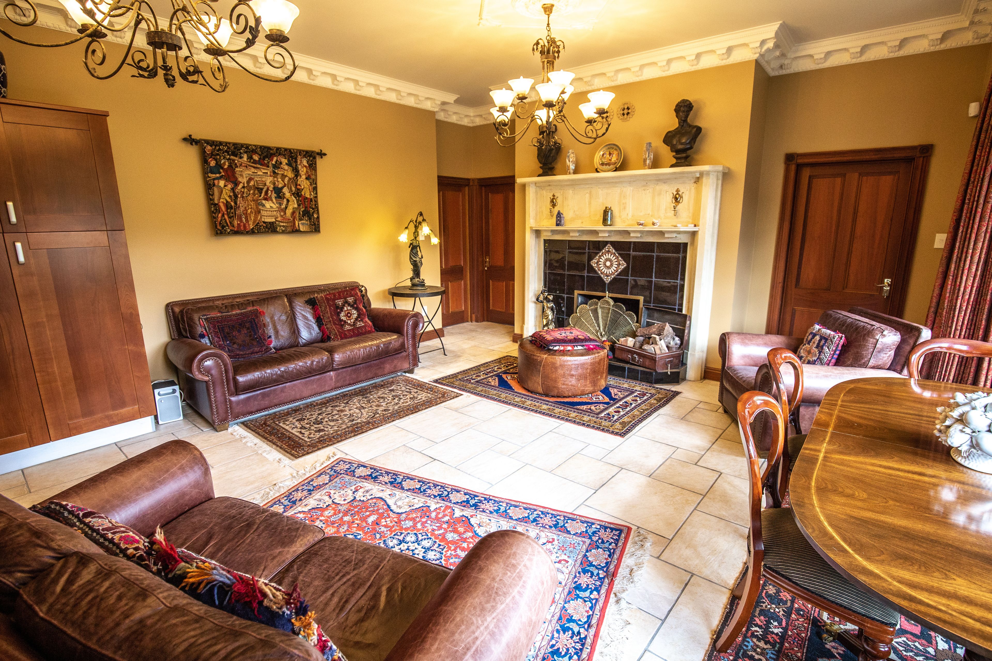 A spacious living room with a fireplace, leather sofas, a dining table, and a chandelier.
