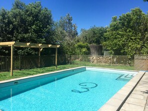 Ein rechteckiger Pool mit einer Holz-Pergola und einer Steinmauer im Hintergrund.