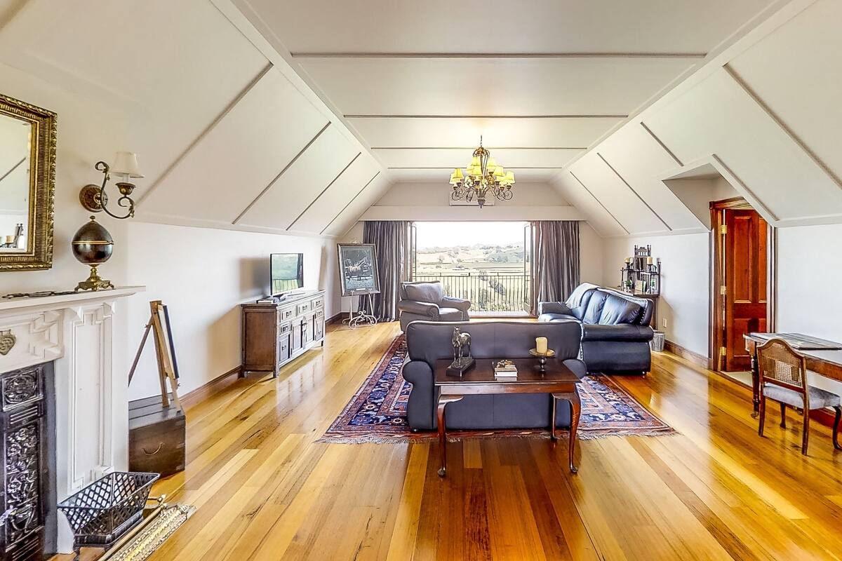 A spacious loft apartment with a high ceiling, a fireplace, a dining area, and a balcony with a view.