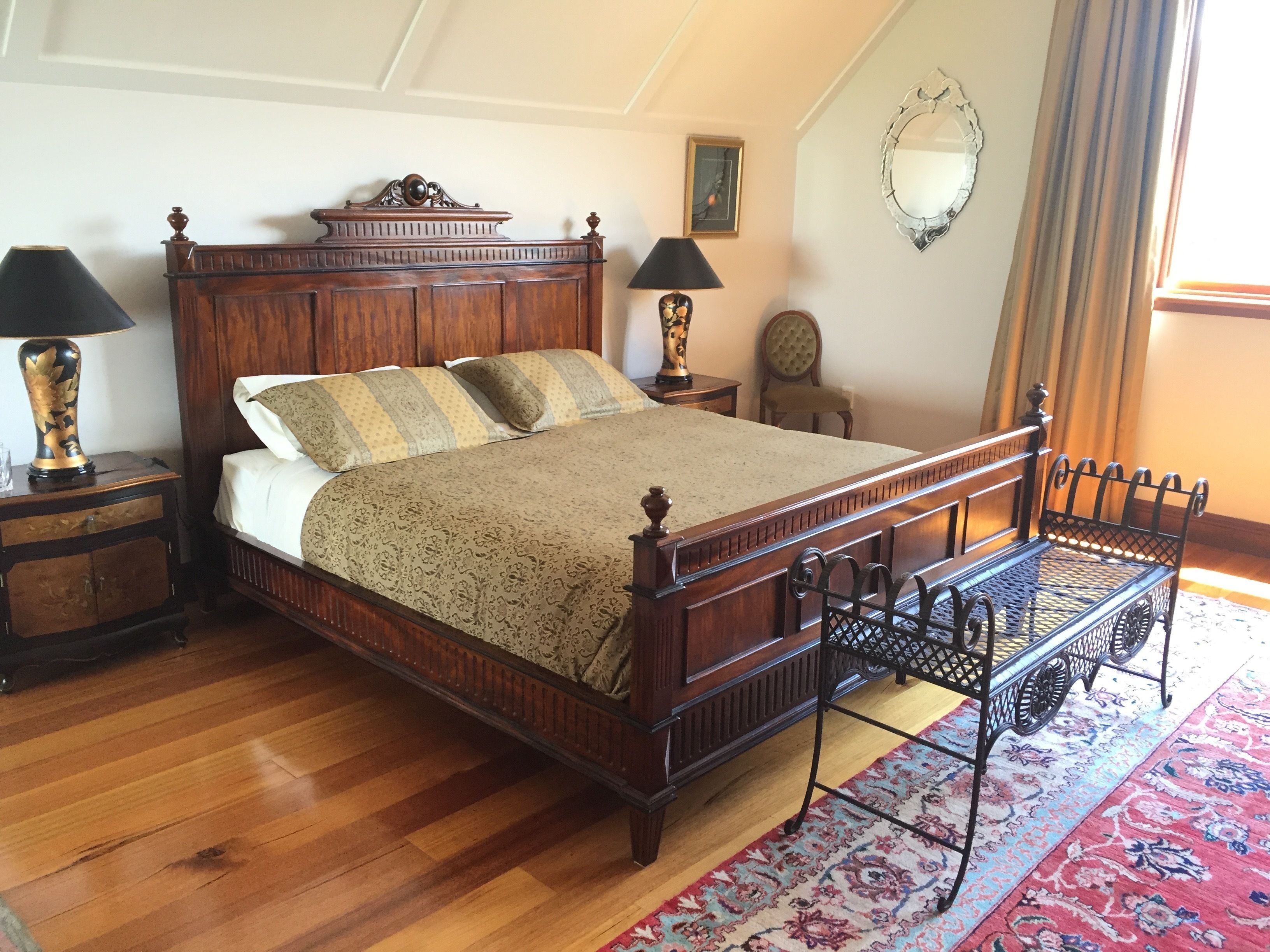 A traditional wooden four-poster bed with a matching nightstand, a small table, and a chair.