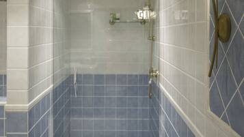 Um chuveiro com porta de vidro, azulejos azuis e luminária fixada na parede.
