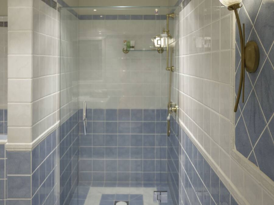 Um chuveiro com porta de vidro, azulejos azuis e luminária fixada na parede.