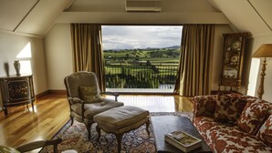 A room with a view of rolling hills, a sofa, a chair, and a table. - Lake Karapiro Lodge (Karapiro)