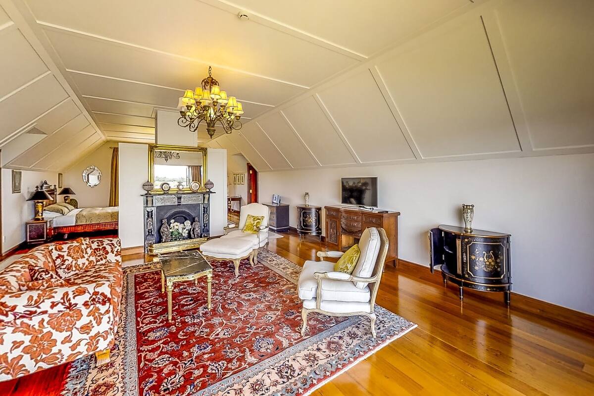 A spacious attic room with a large, ornate chandelier, a fireplace, and a variety of seating options including a sofa and armchairs.