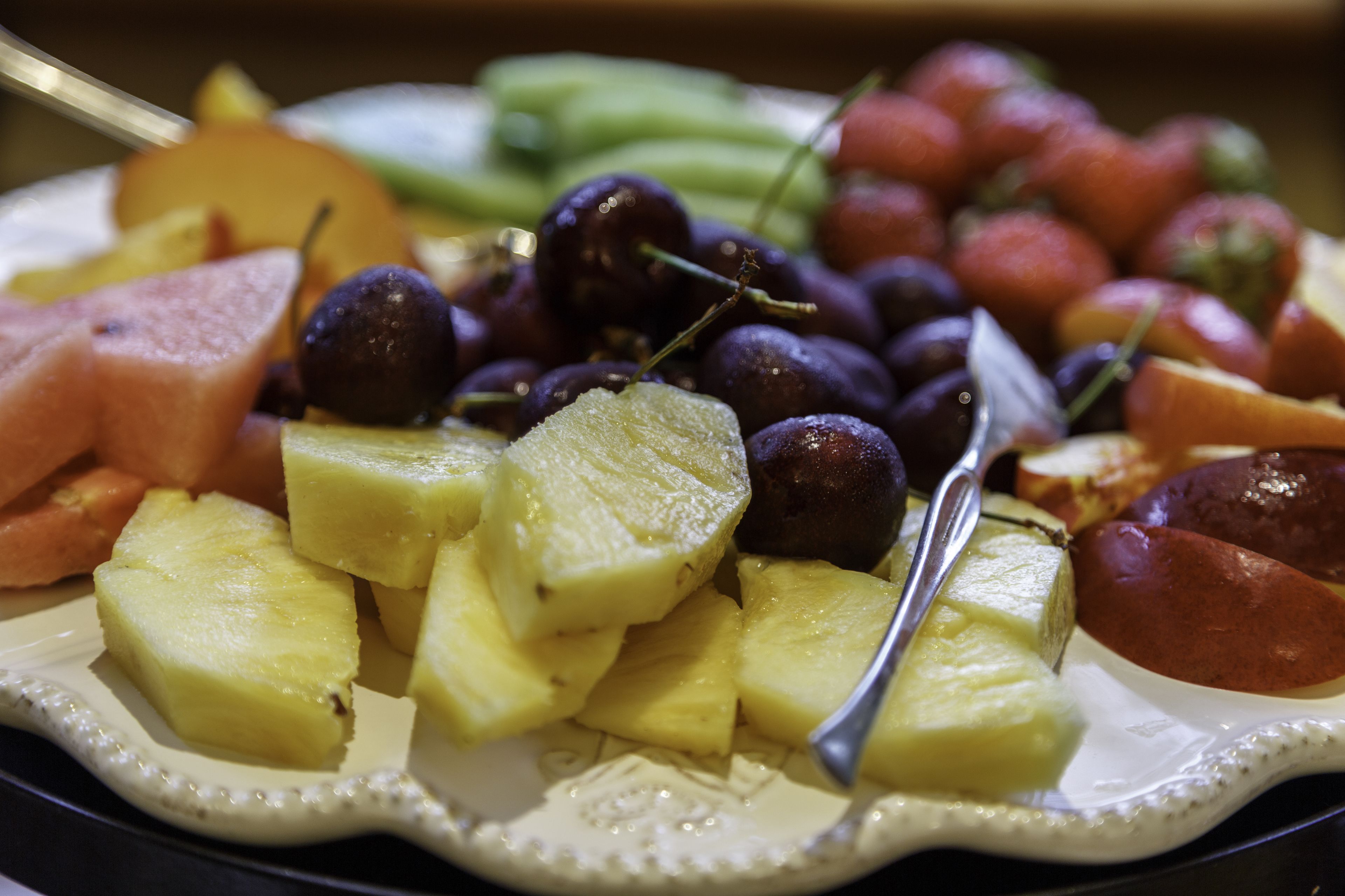 En tallerken med forskelligt frugt, heraf druer, æbler og ananasstykker.