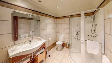 Un baño moderno con un espejo grande, un lavamanos con pileta, un inodoro y una zona de ducha con mampara de vidrio.