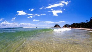 A beach with clear shallow waters, a sandy shore, and a distant island. - Reflections Byron Bay - Holiday Park (Byron Bay)