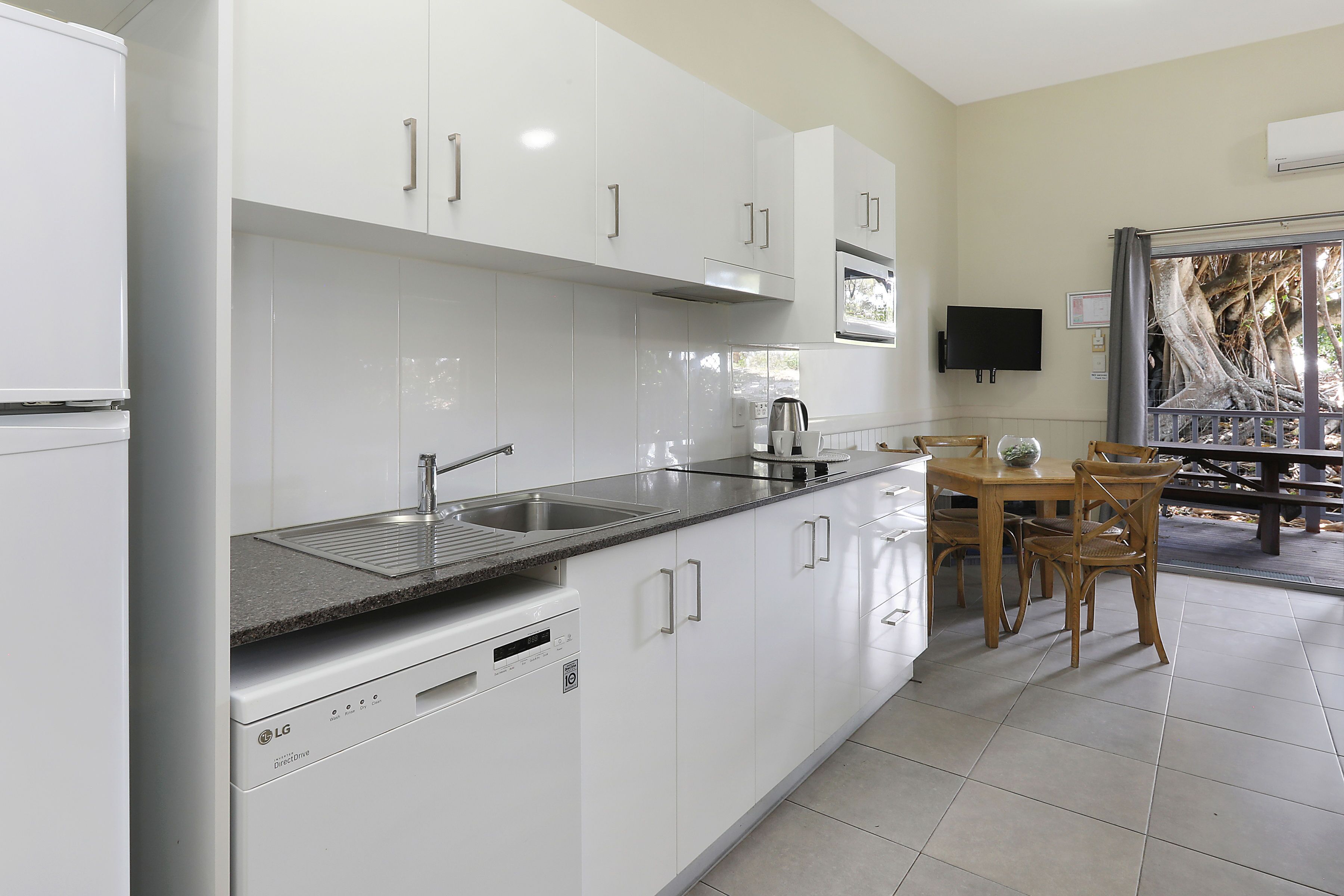 A modern kitchen with white cabinets, a built-in dishwasher, a granite countertop, and a dining area with wooden chairs and a table.
