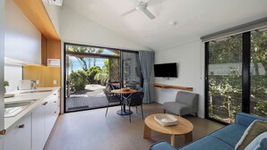 A modern living room with a sofa, coffee table, and a dining area with a table and chairs. - Reflections Byron Bay - Holiday Park (Byron Bay)