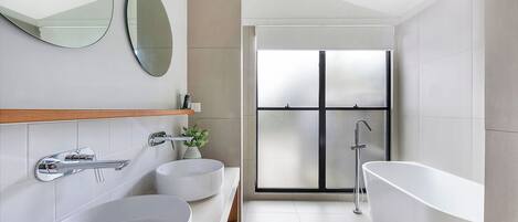 A modern bathroom with two sinks, a large mirror, and a freestanding bathtub.