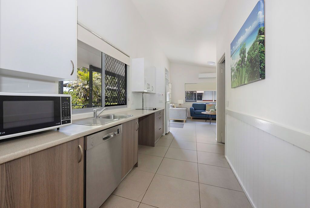 A modern kitchen with a microwave, sink, and dishwasher. A hallway leads to a living area with a blue sofa and a painting of a landscape.