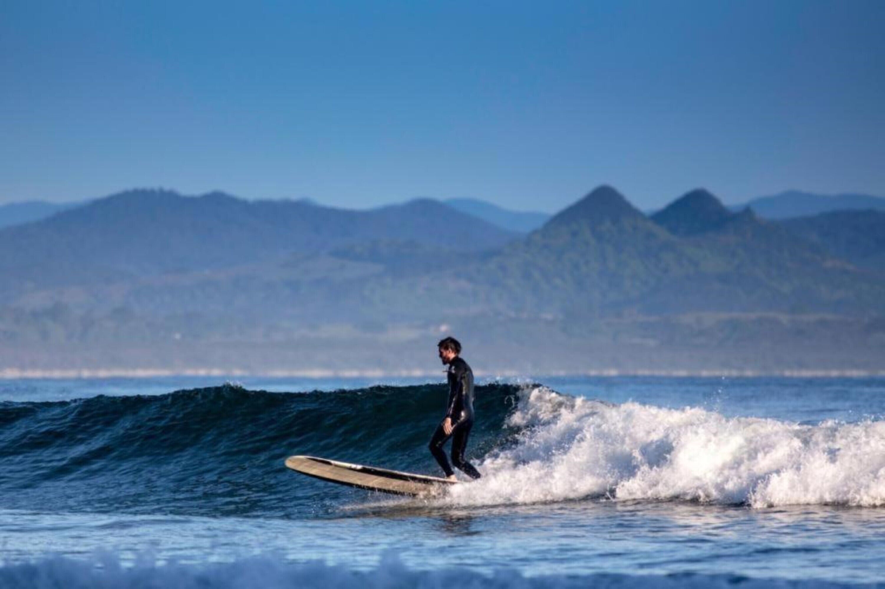 Un surfeur surfe sur une vague, avec des montagnes en arrière-plan.