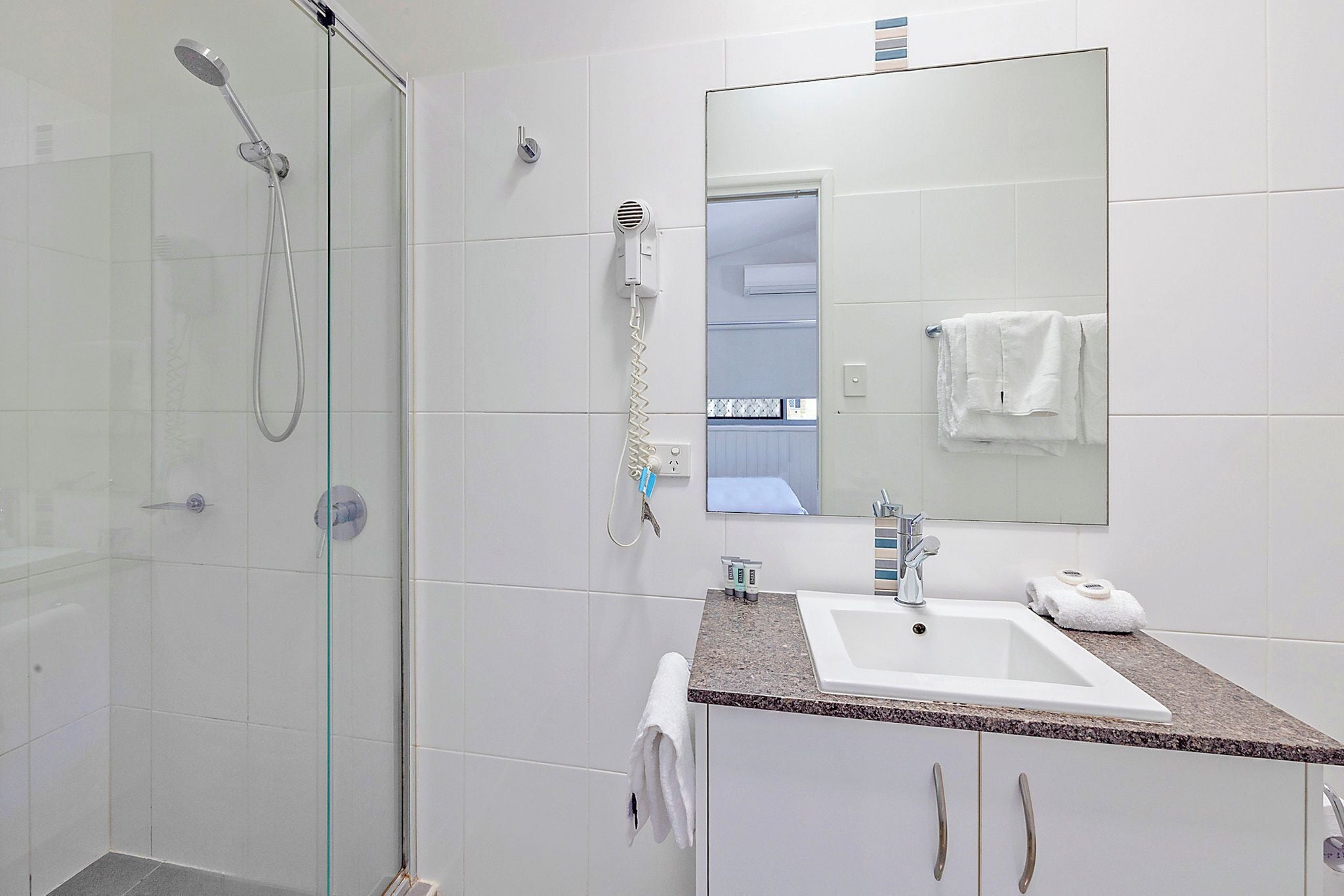 A modern bathroom with a glass-enclosed shower, a sink with a marble countertop, and a large mirror above the sink.