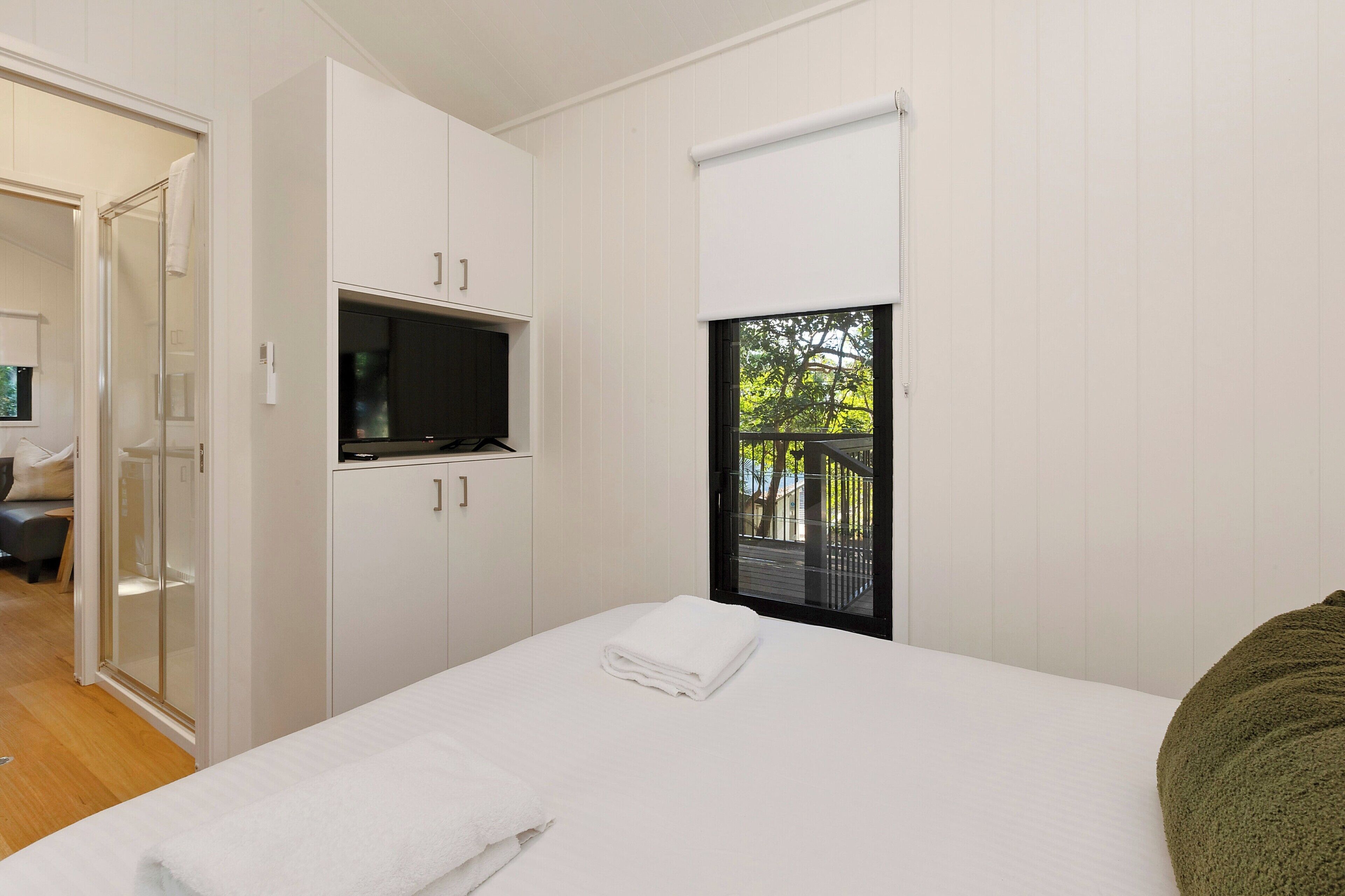 A bedroom with a bed, a TV, a window with a view, and a door leading to a balcony.