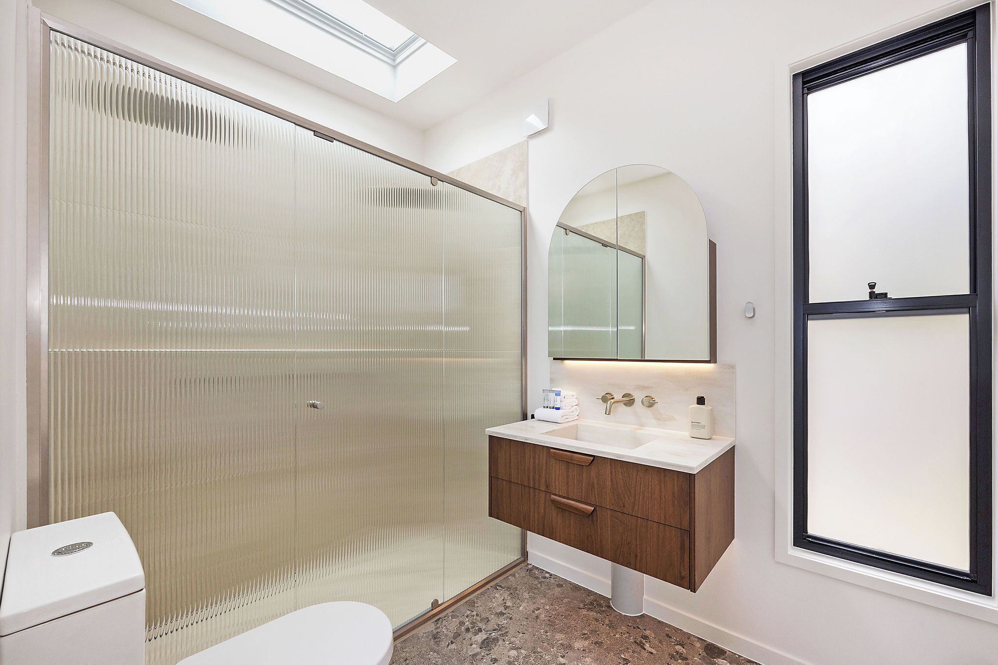 Een moderne badkamer met een douchecabine van glas, een witte wastafel met houten meubel, en een grote spiegel erboven.