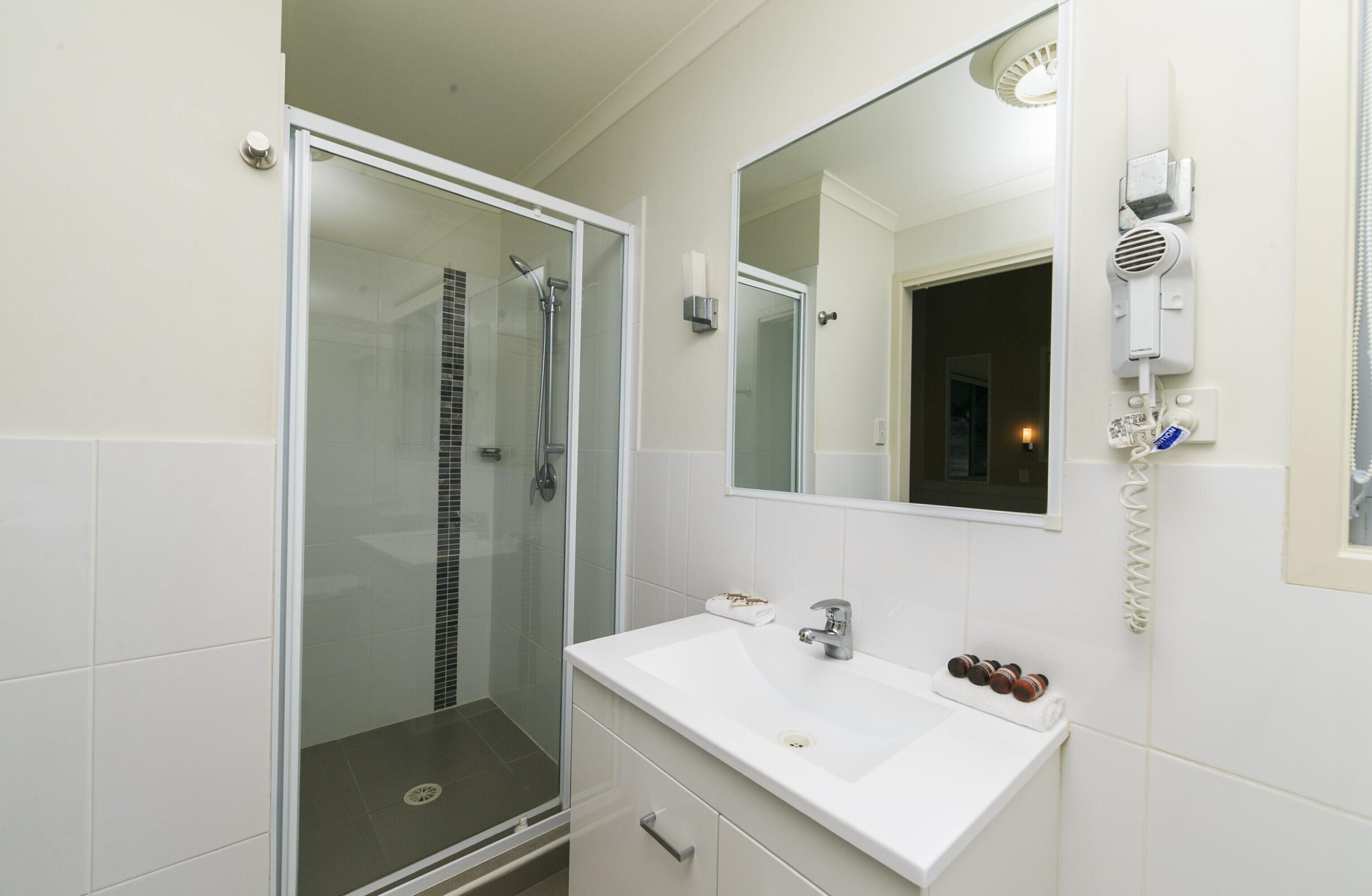 A bathroom with a glass shower enclosure, a white sink, a mirror, and a hairdryer mounted on the wall.