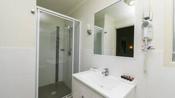 A bathroom with a glass shower enclosure, a white sink, a mirror, and a hairdryer mounted on the wall.