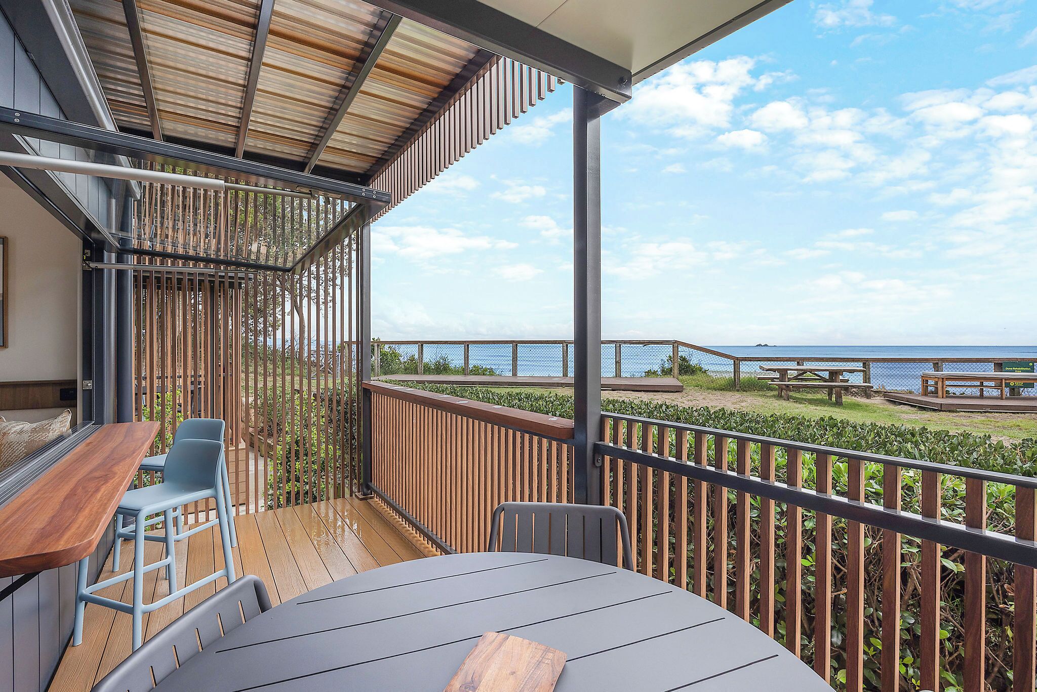 A covered outdoor area with a wooden deck, a table with chairs, and a view of the sea.