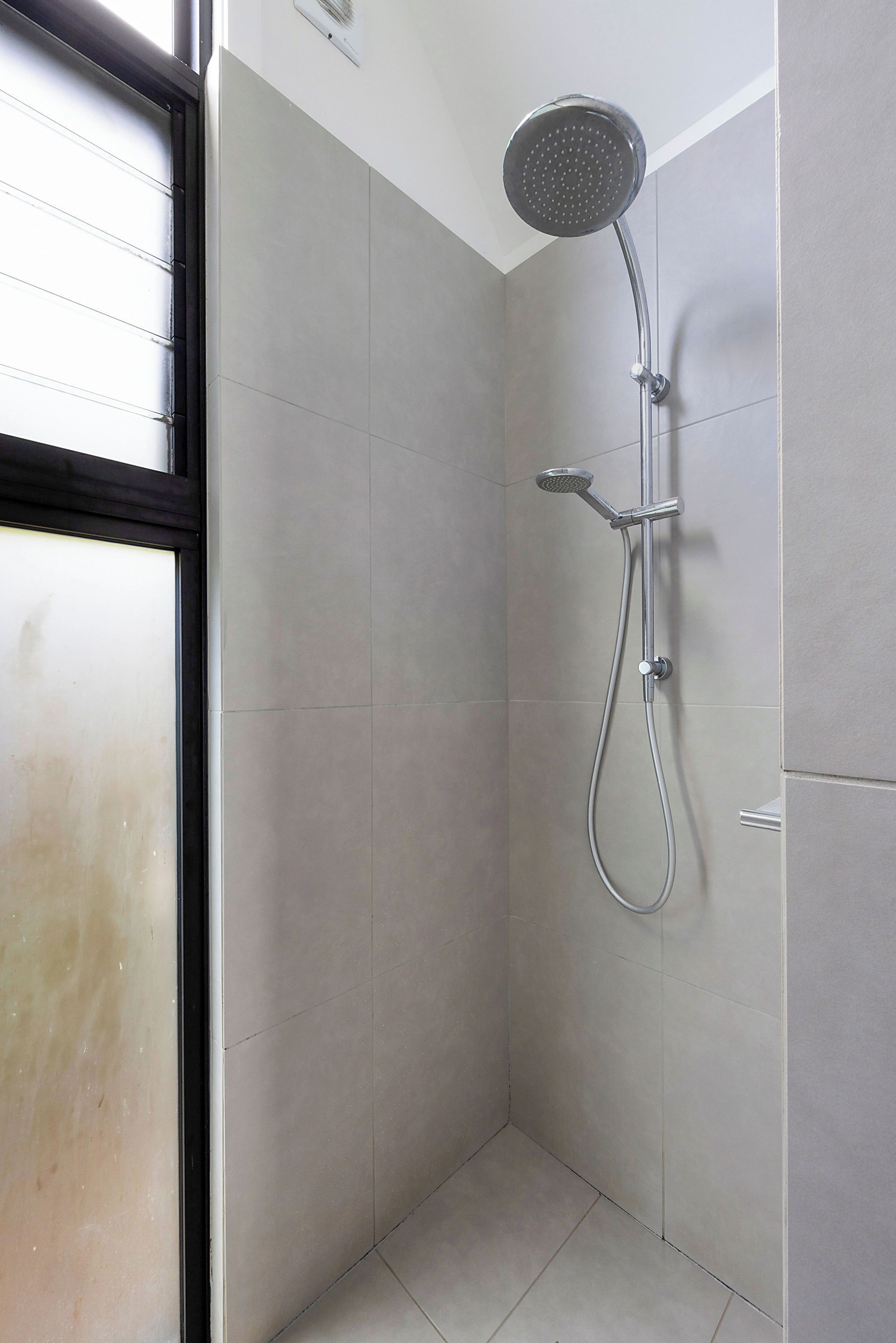 A shower with a handheld showerhead and a wall-mounted faucet in a corner of a room with tiled walls and a window.