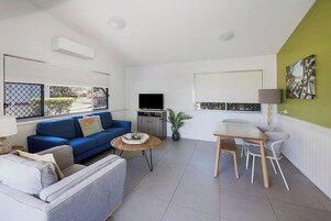 Una sala de estar moderna con un sofá azul, un sillón gris, una mesa de centro de madera y un comedor con mesa y sillas.
