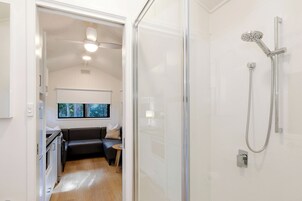 A modern bathroom with a glass shower enclosure, a ceiling fan, and a view of a living area with a sofa and a small table.