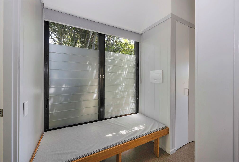 A room with a bench under a sliding glass door, white walls, and a door to the right.