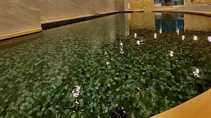 Piscina interna com água cristalina, teto de madeira e paredes de pedra.
