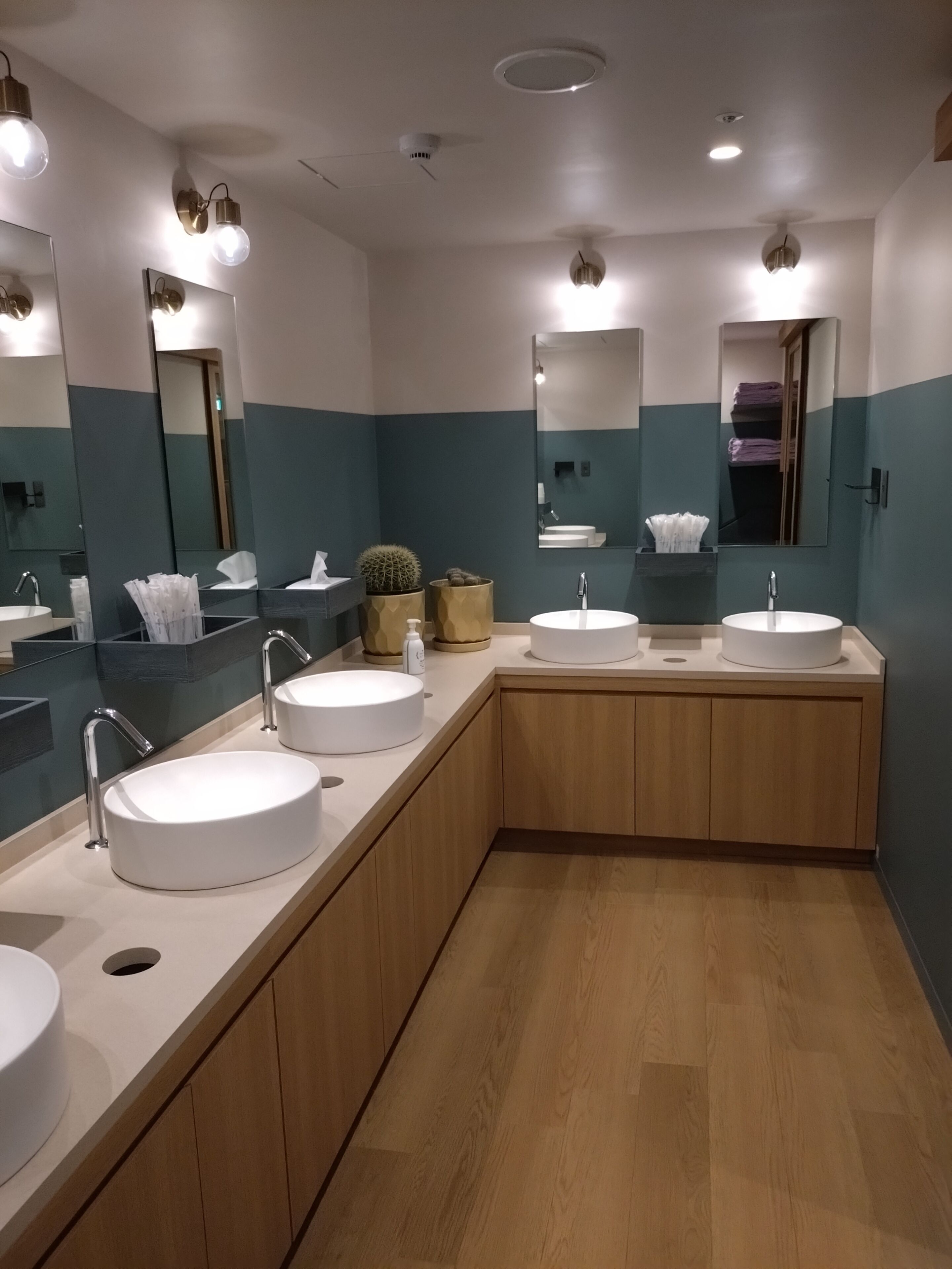 A modern bathroom with three sinks, wooden cabinets, and a large mirror.