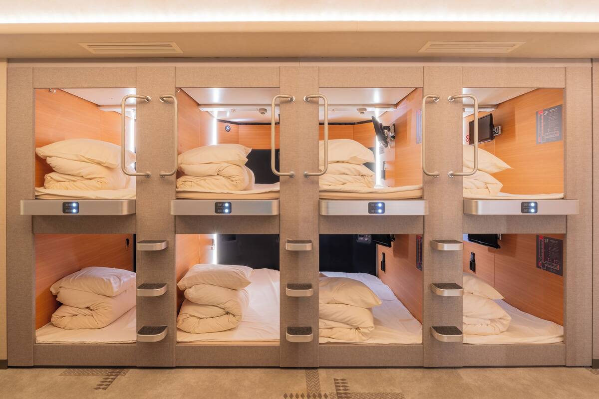 A train compartment with four berths, each with a bed, pillows, and a control panel.