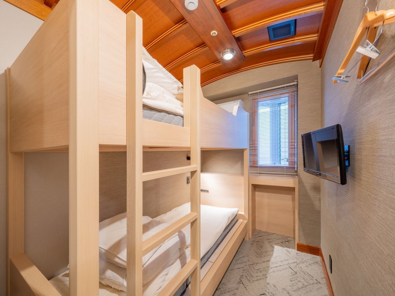 A bunk bed room with a TV mounted on the wall and a window with blinds.