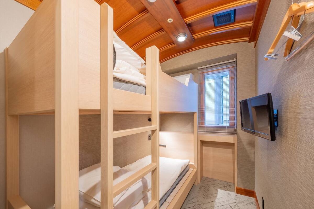 A bunk bed room with a TV mounted on the wall and a window with blinds.