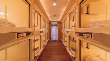 A hotel corridor with bunk beds, numbered room signs, a carpeted floor, and a curtain at the end.