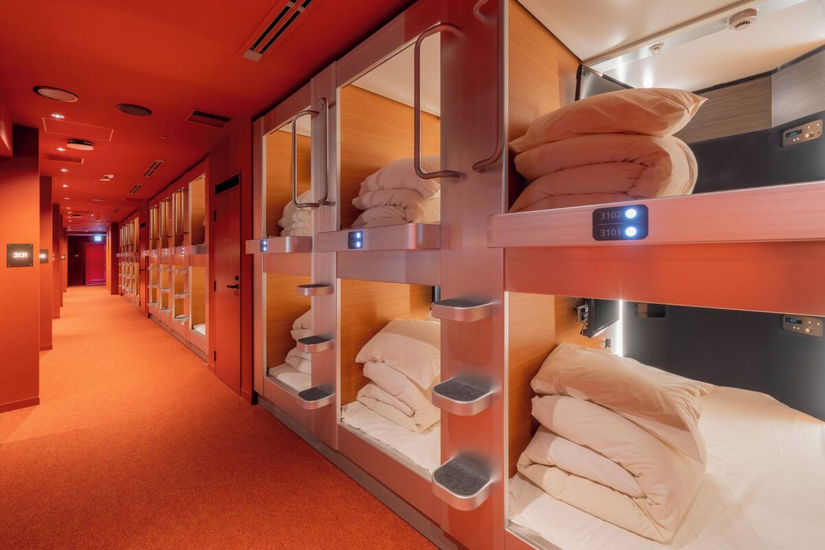 A hotel corridor with bunk beds, each with a control panel and a small shelf.