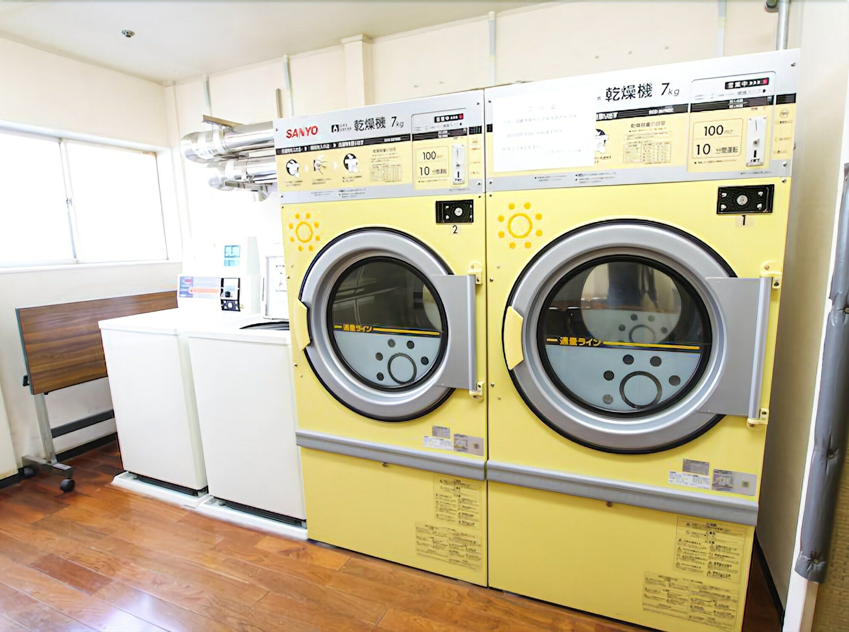 A laundry facility with two yellow machines, a white counter, and a wooden bench.