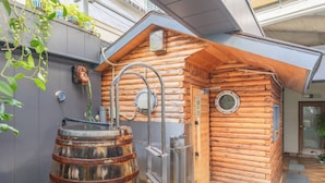 Uma cabana rústica de madeira com sauna, um barril de metal e uma pequena janela.