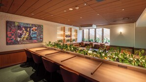 Uma sala de conferência com uma longa mesa de madeira, cadeiras, plantas em vasos e uma grande pintura abstrata na parede.