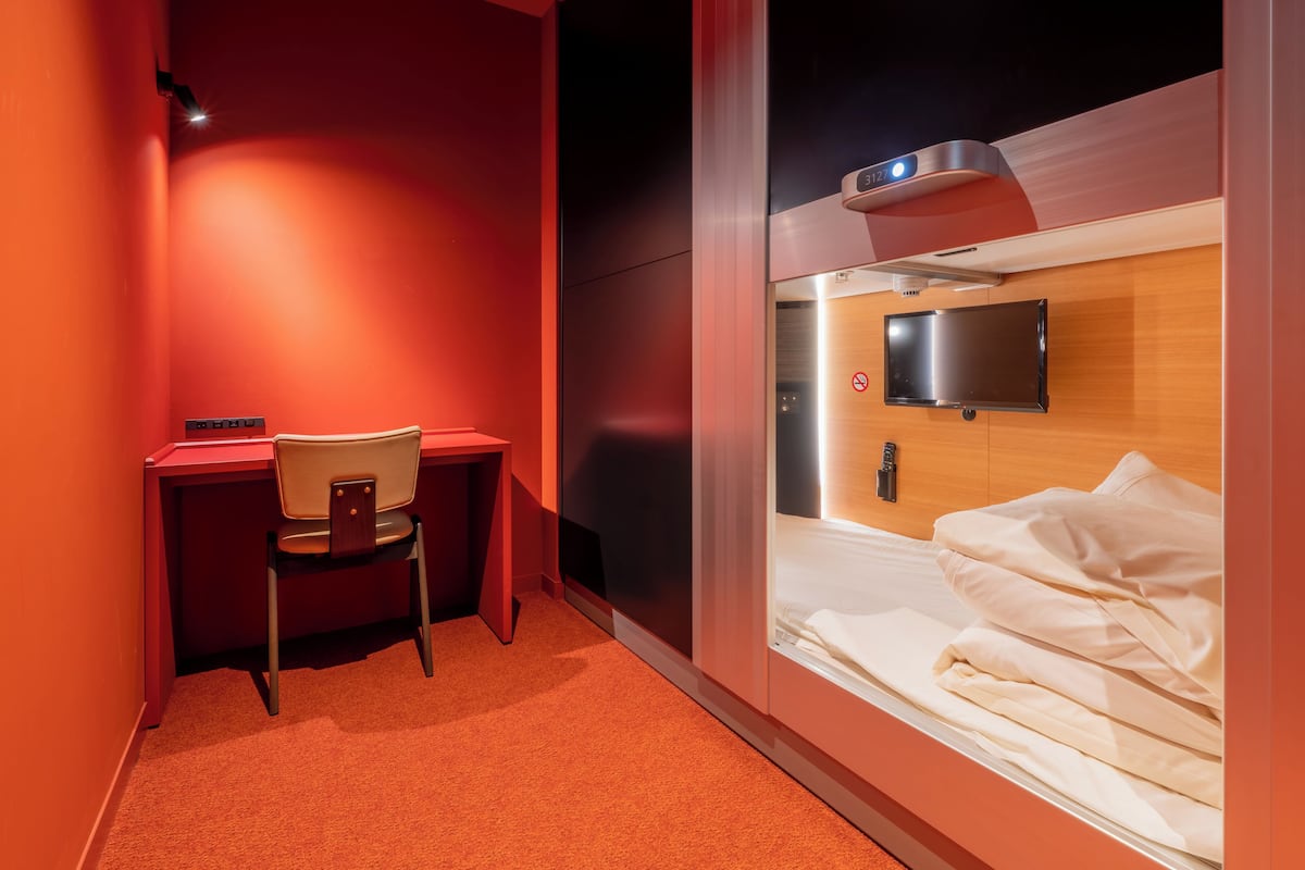 A hotel room with a bed, a desk, a chair, a TV, and a red wall.