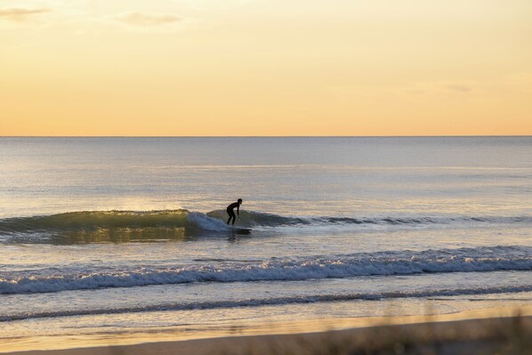A person surfing on a wave at sunset.
