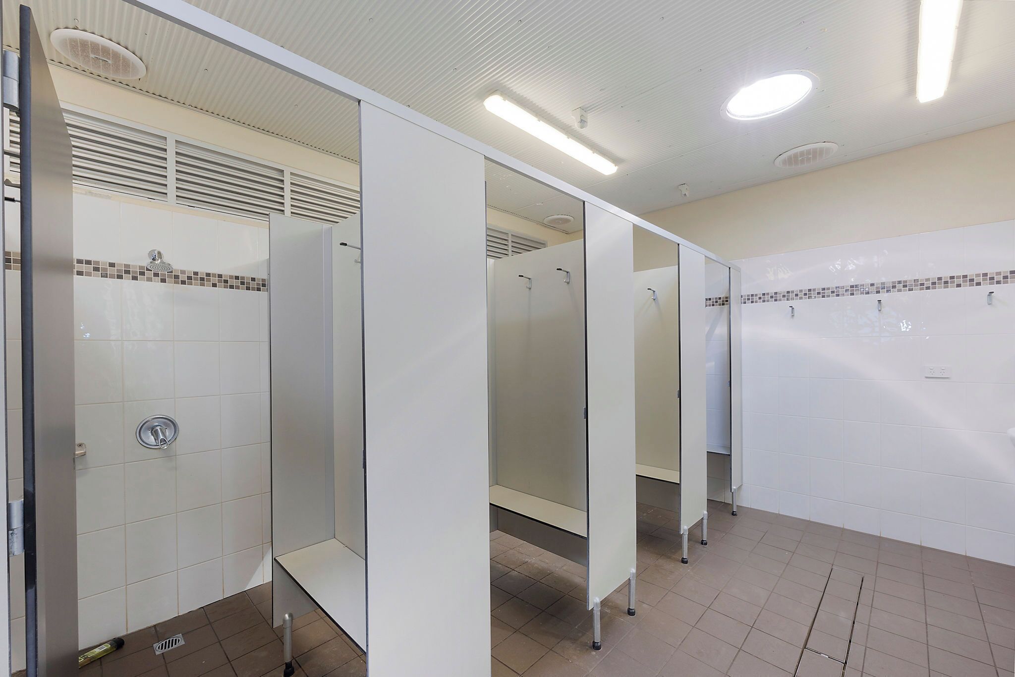 A restroom with multiple stalls, a tiled floor, and a ceiling with recessed lighting.