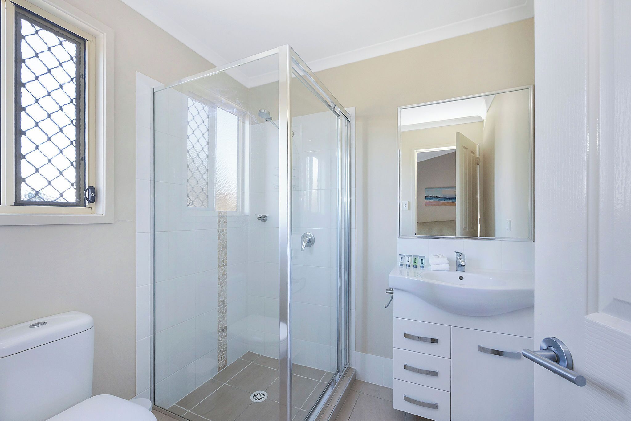 A modern bathroom with a glass shower enclosure, a white sink, and a mirror above the sink.