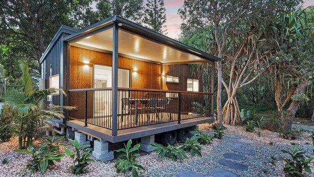 Une cabane moderne dotée d’une terrasse en bois, de grandes fenêtres et d’un chemin en pierre menant à l’entrée.