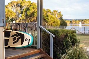 A surfboard on a wooden deck with a railing, a view of a lake, and a fence in the background.